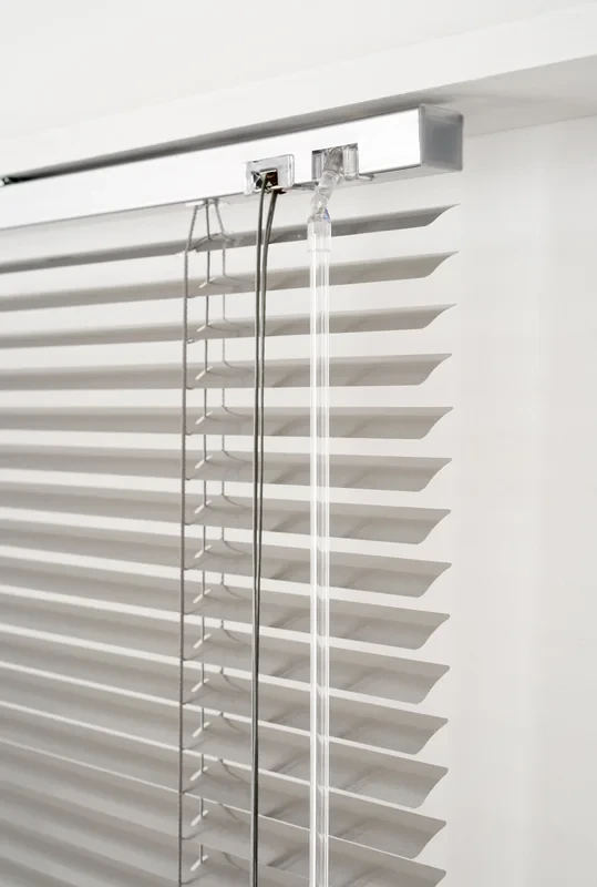 Detail of a silver 25 mm aluminium venetian headrail end: tilter, lift cord and clear hollow wand, silver slats