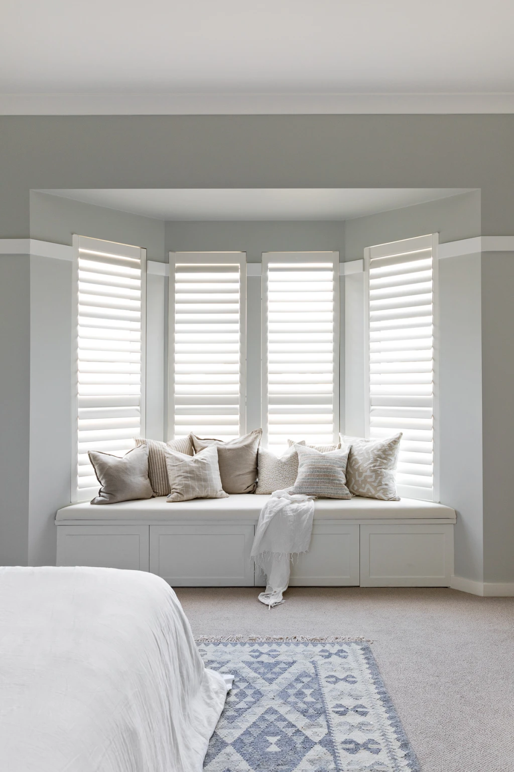 White plantation shutters across a bay window above a window seat