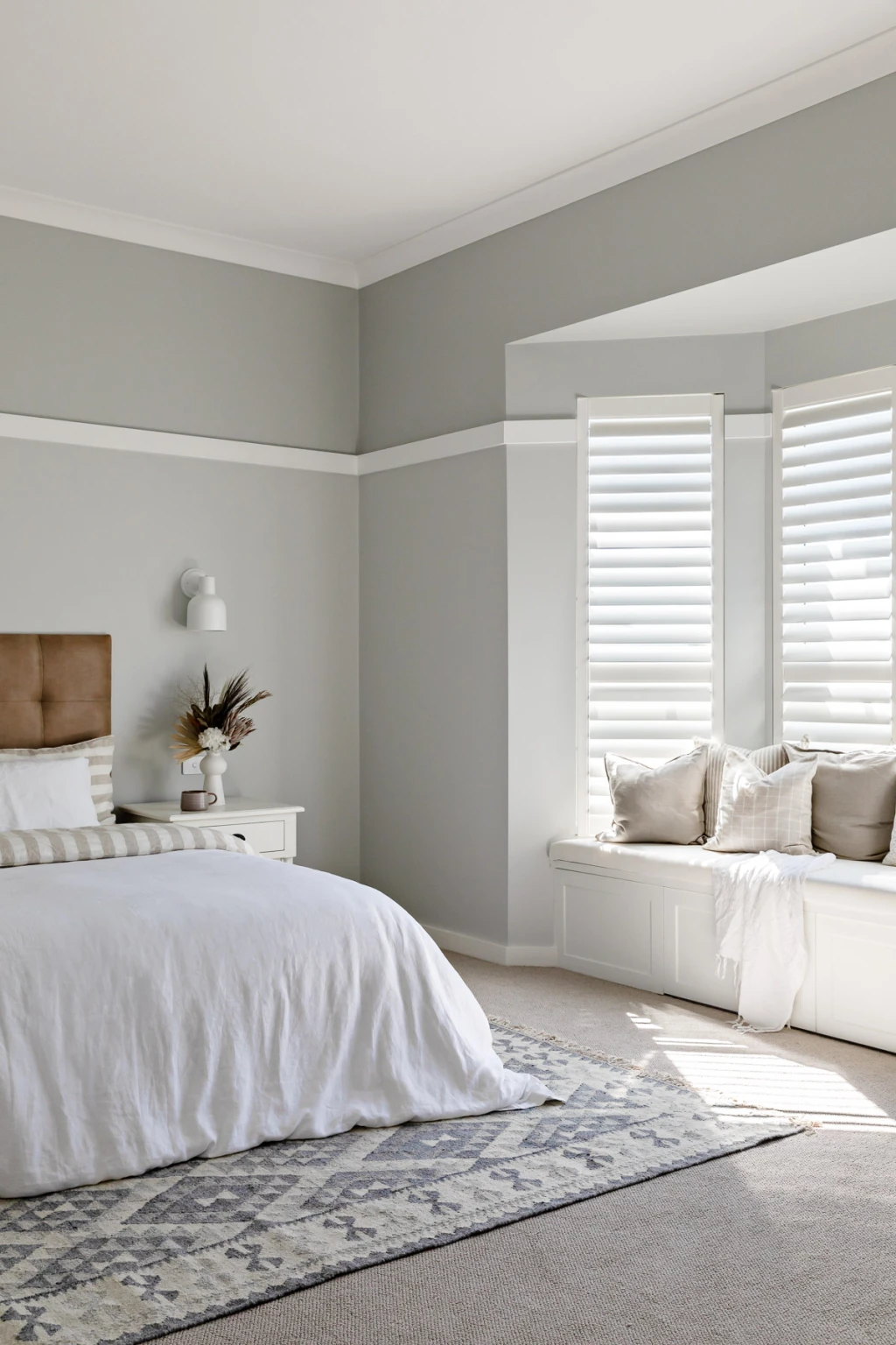 White plantation shutters on a bay window beside a bed