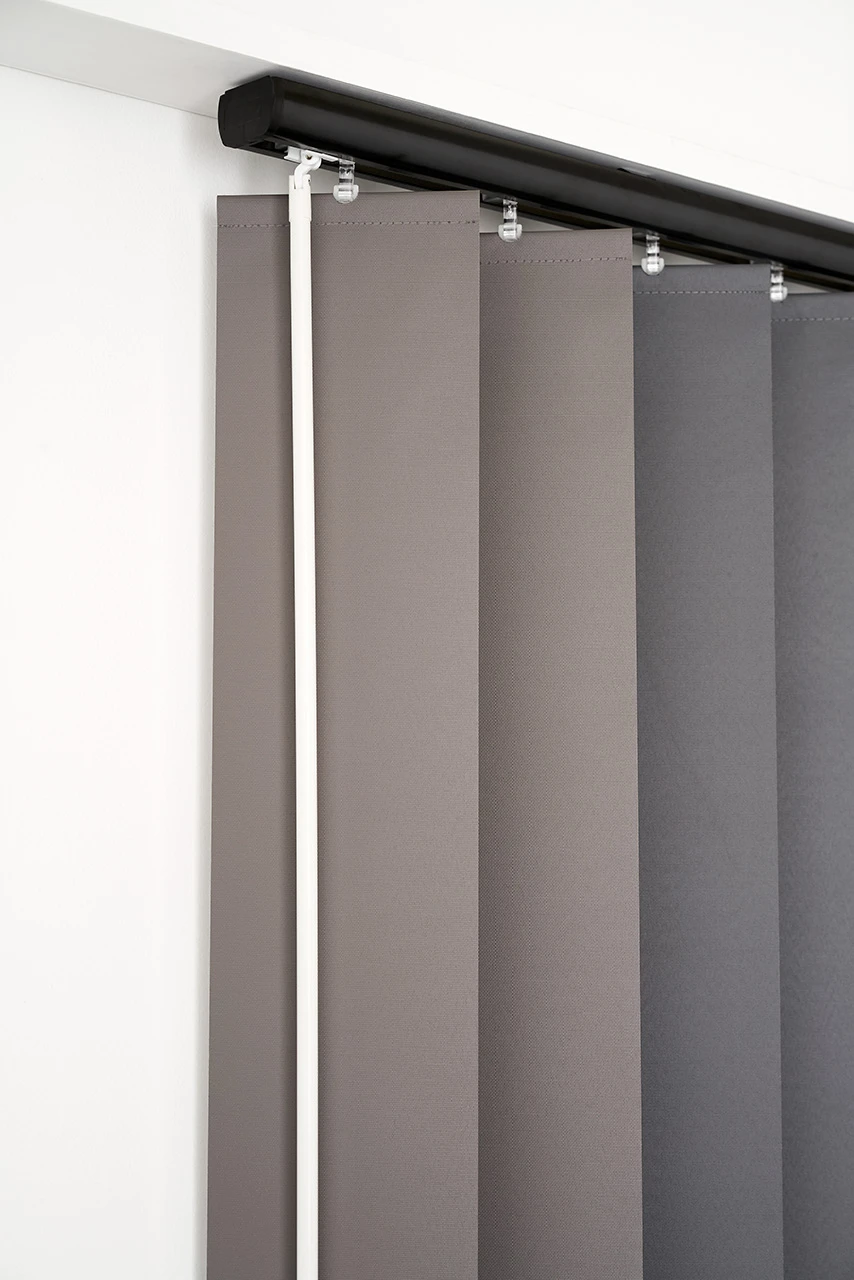 Grey vertical blind vanes hanging from a black track, with a white wand