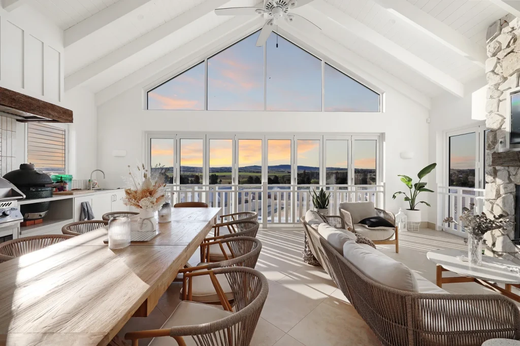 Open-plan living and dining room with a raked ceiling and blinds on the tall windows