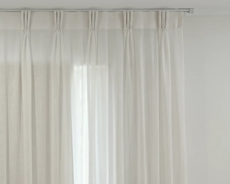 Close-up of a white sheer triple pinch pleat curtain heading hanging from a white ceiling track