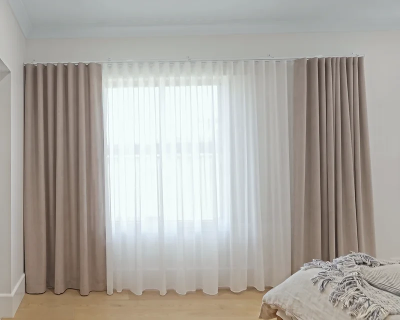 Double curtains on wall-fixed tracks above a window: white sheer closed, taupe blockout drawn open