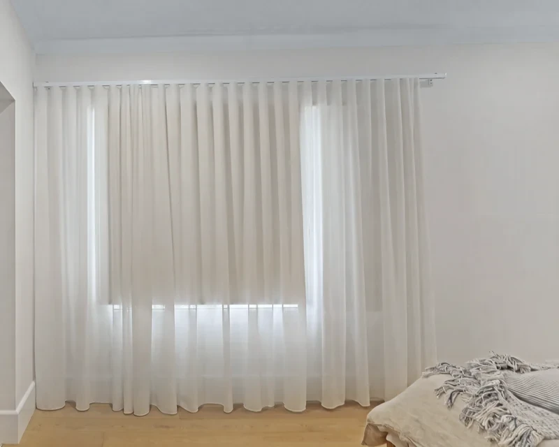 White sheer S-fold curtain on a track fixed to the wall above the window, falling to the floor