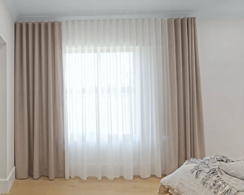 Double curtains on ceiling tracks: white sheer closed across the window, taupe blockout drawn open
