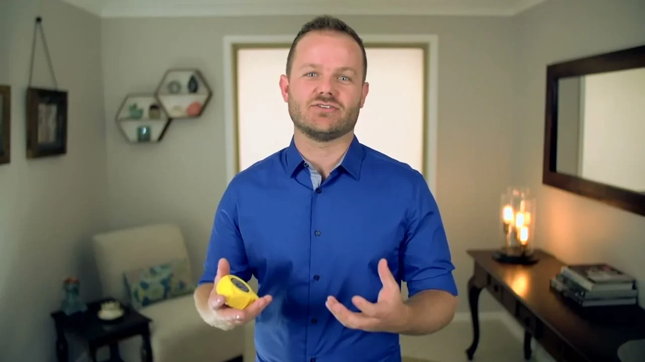 Presenter holding a yellow steel tape measure at the start of our how to measure for blinds video