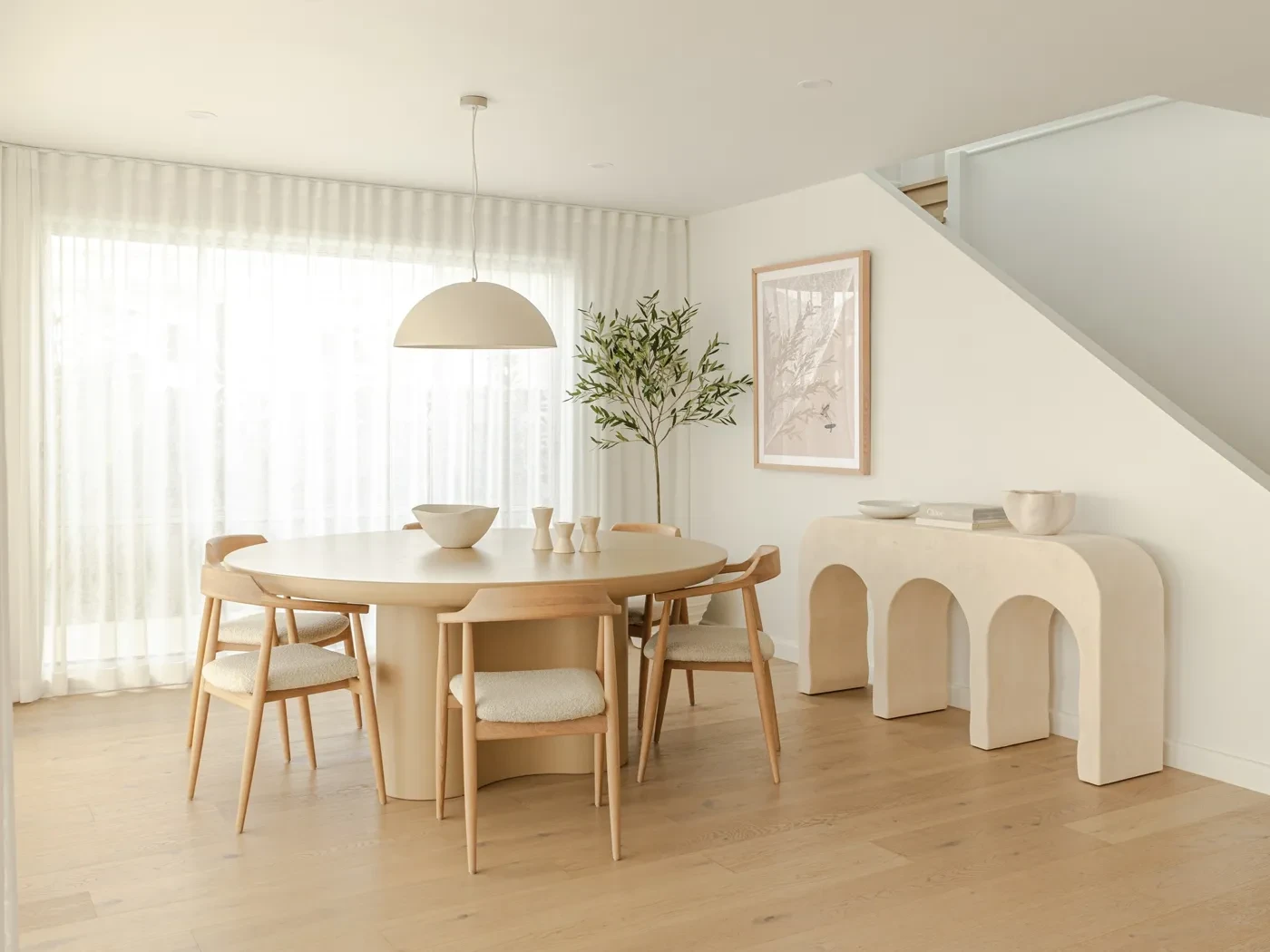 Dining room in HAAUS.7 with floor-length sheer curtains behind a round timber table