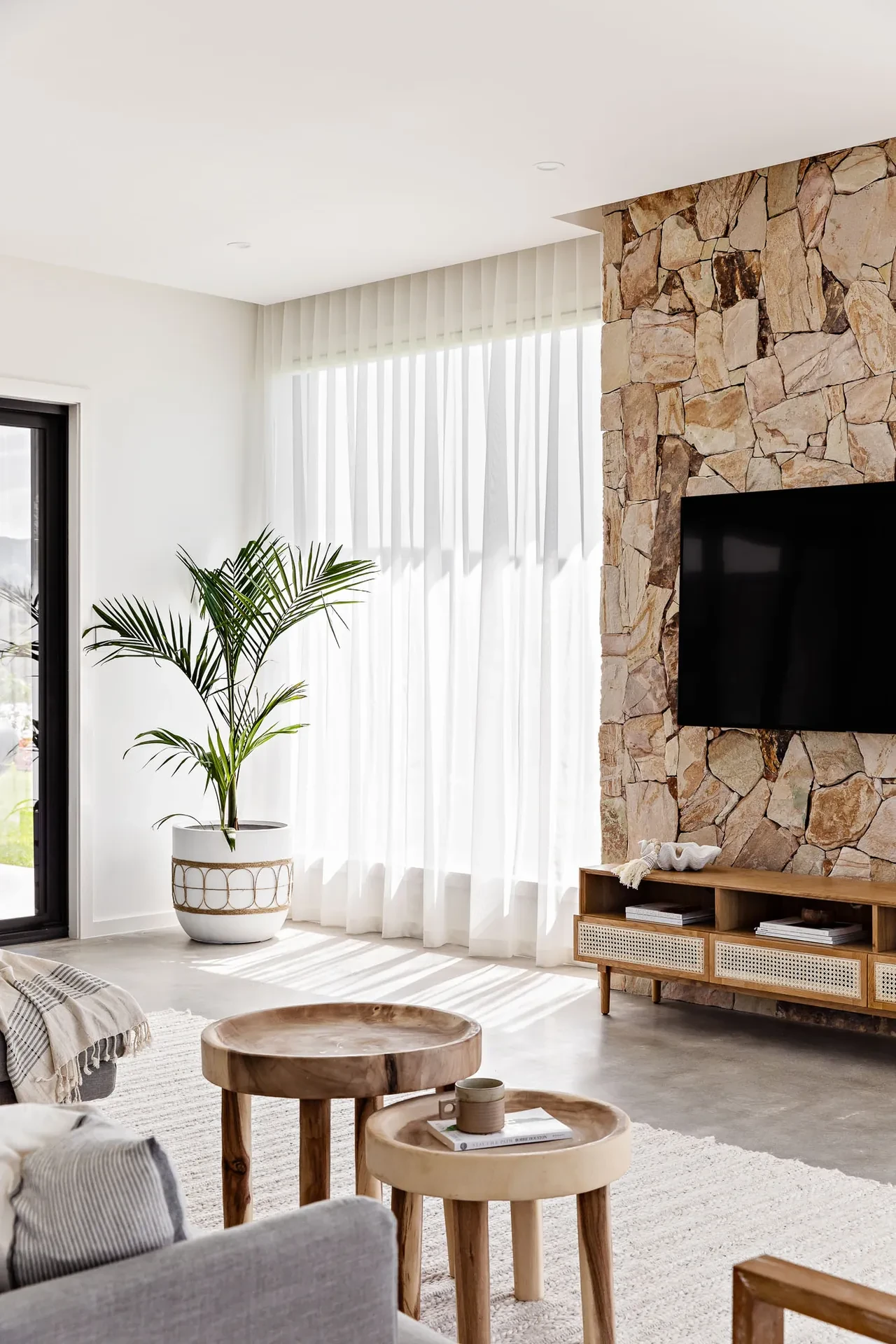 A wall of white S-fold sheer curtains on a ceiling track beside a stone feature wall A wall of white S-fold sheer curtains on a ceiling track beside a stone feature wall