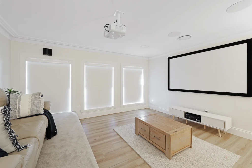 Three white blockout roller blinds, fully lowered and recess-fitted, in a media room