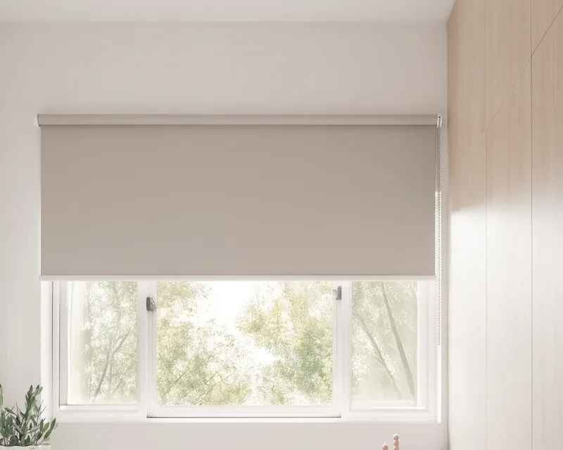 Light grey roller blind fixed to the wall above a study window, covering the window frame, chain on the right