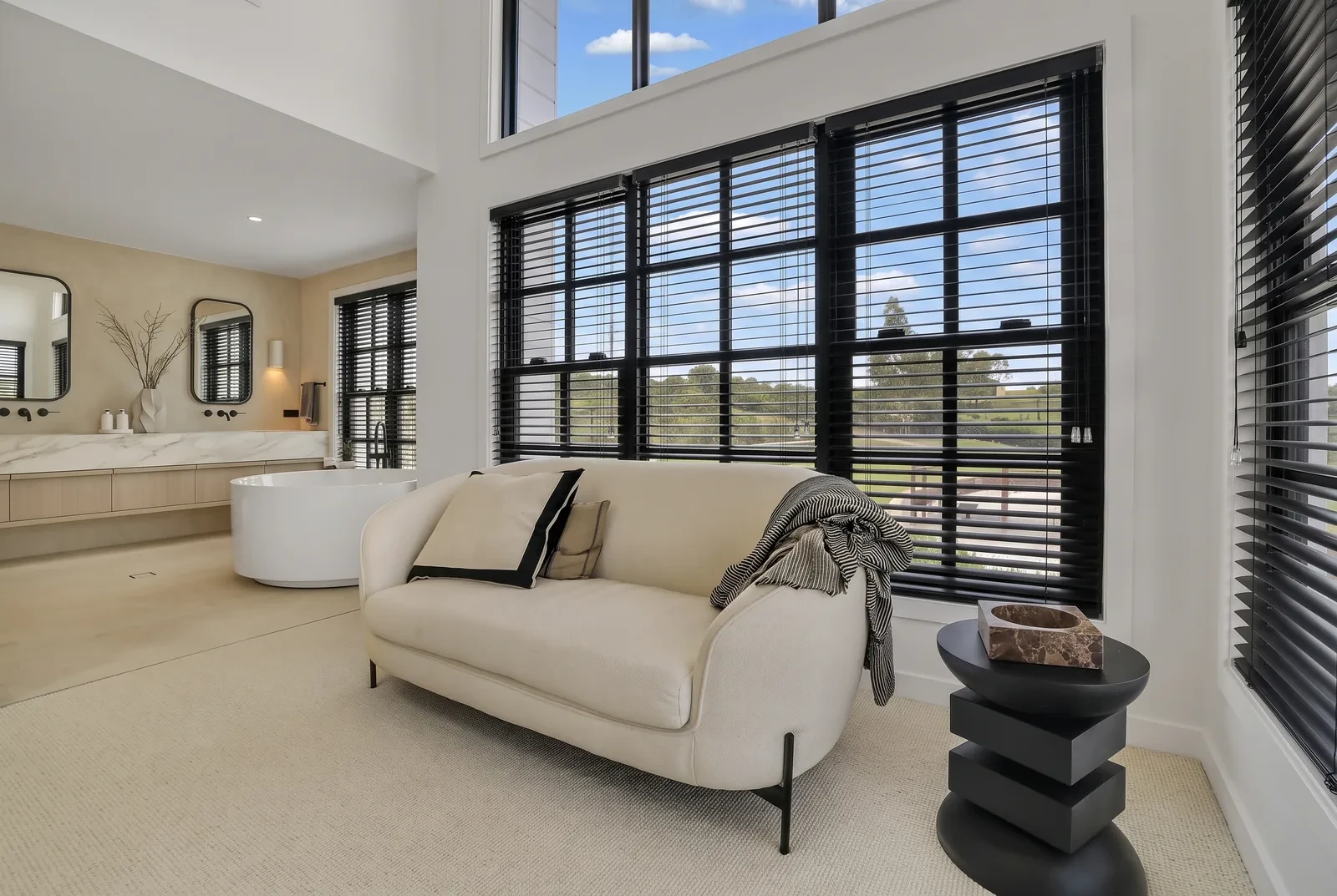 Black 50mm aluminium venetian blinds on tall black-framed bathroom windows beside a freestanding bath