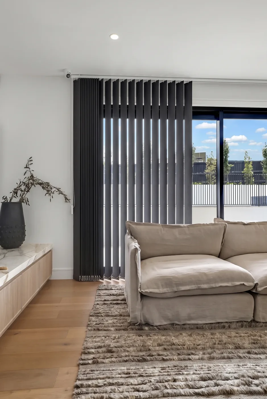 Charcoal fabric vertical blinds drawn across a living room sliding door, vanes half open