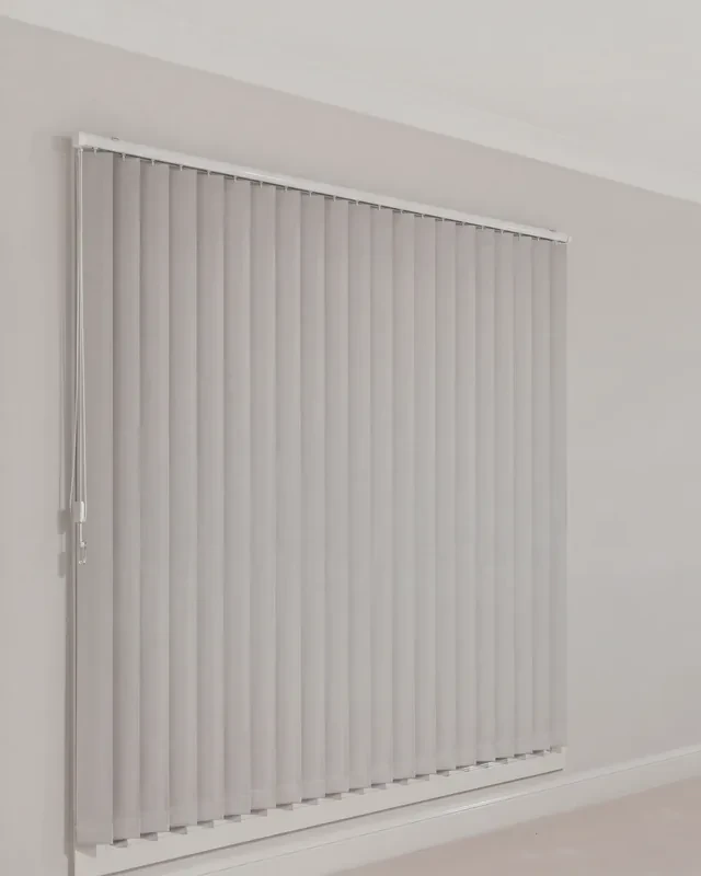 Light grey vertical blind fixed to the wall above a window, opaque blockout vanes closed, square-cut chainless hems, no chain