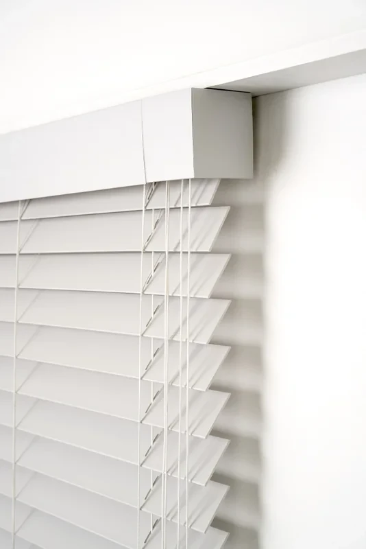 Detail of a white Visionwood PVC venetian fascia corner with its end return, ladder cords and slats below