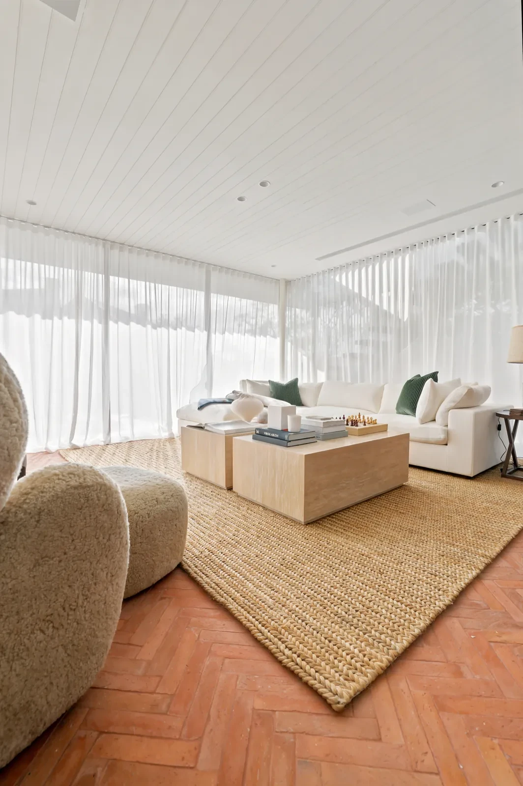 Sheer curtains on ceiling track behind a lounge and jute rug