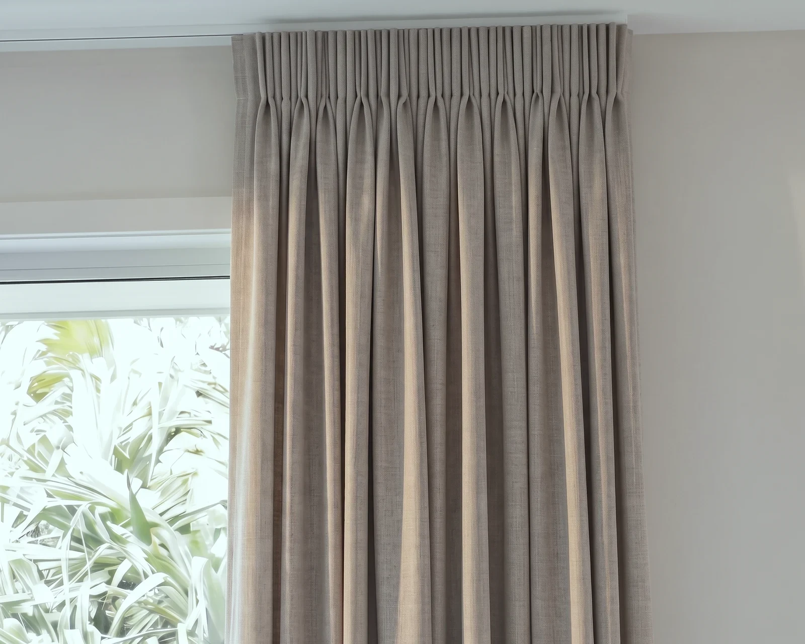 Close-up of a taupe blockout curtain with a pencil pleat heading under a white ceiling track, beside a window
