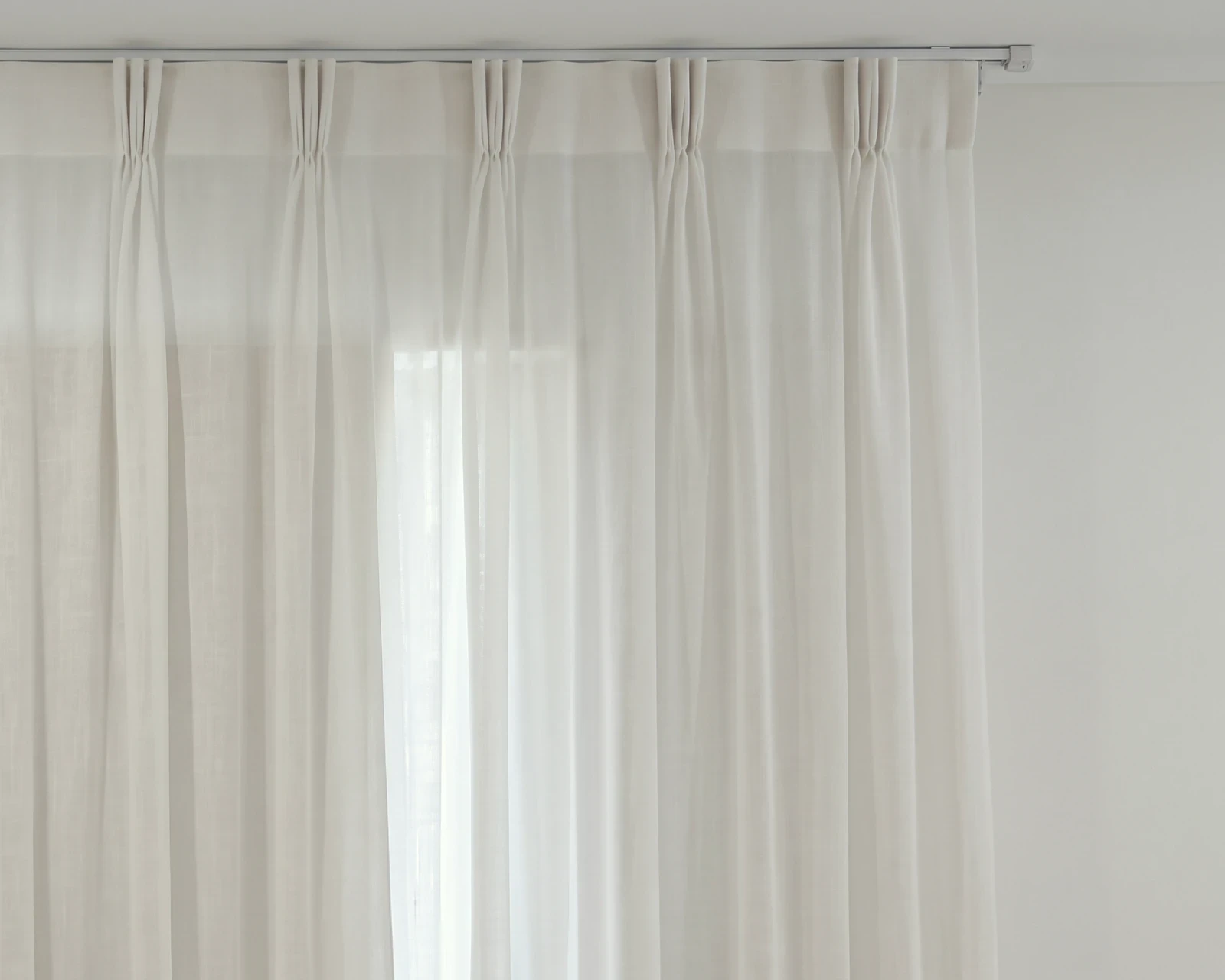 Close-up of a white sheer triple pinch pleat curtain heading hanging from a white ceiling track