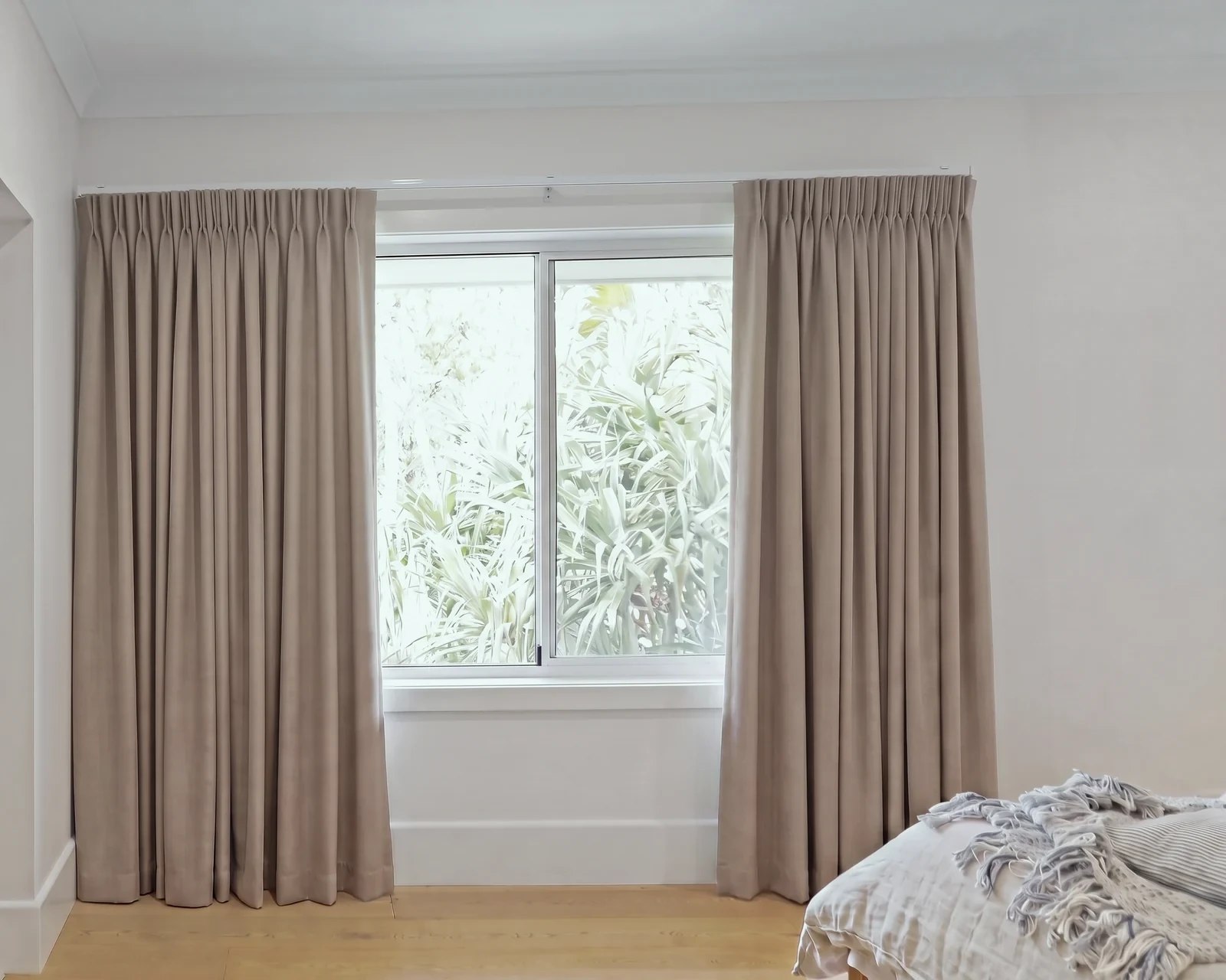 Taupe blockout pencil pleat curtains on a track fixed to the wall above a window, drawn open