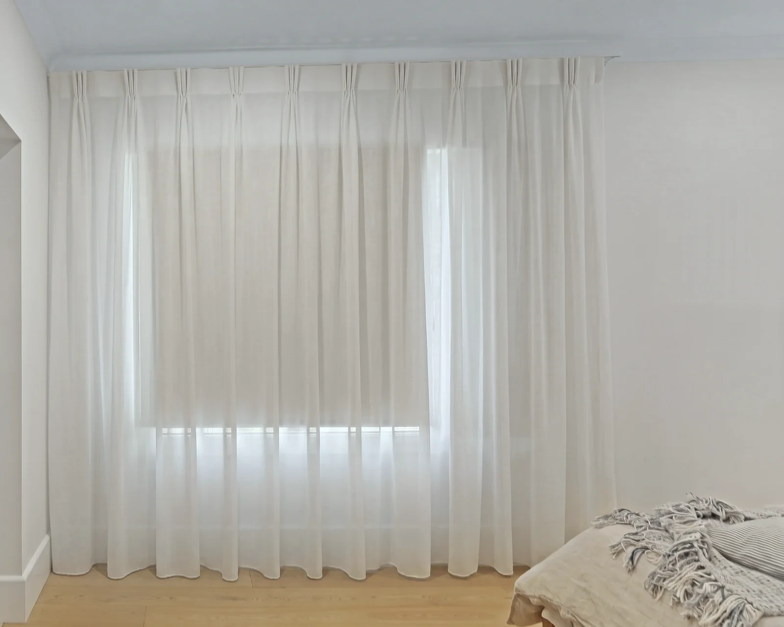 White sheer triple pinch pleat curtain hanging from a ceiling track across a bedroom window