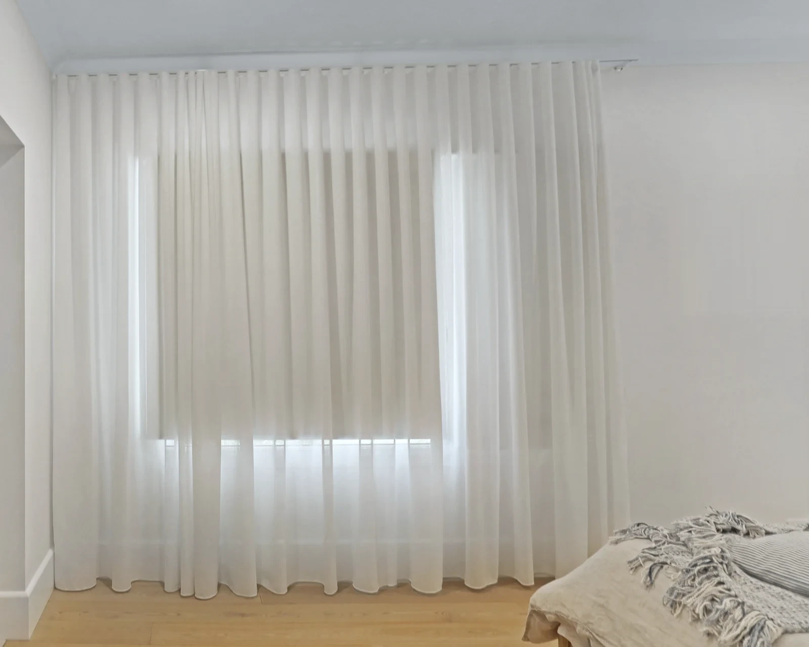 White sheer S-fold curtain hanging from a ceiling track to the floor across a bedroom window