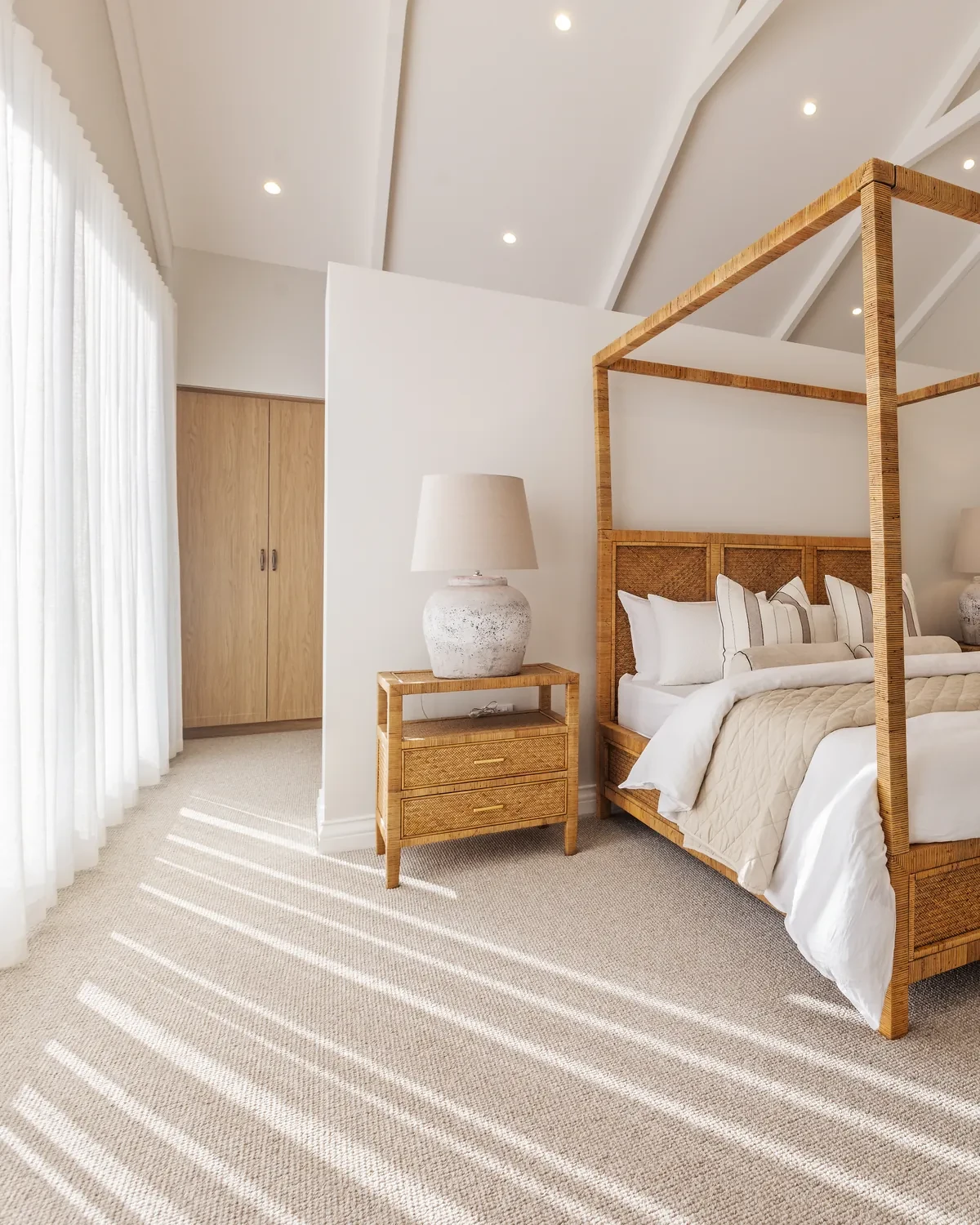 Main bedroom in the Ashbourne display home: Vevey Vanilla S-Fold sheers beside a timber four-poster bed under a raked ceiling