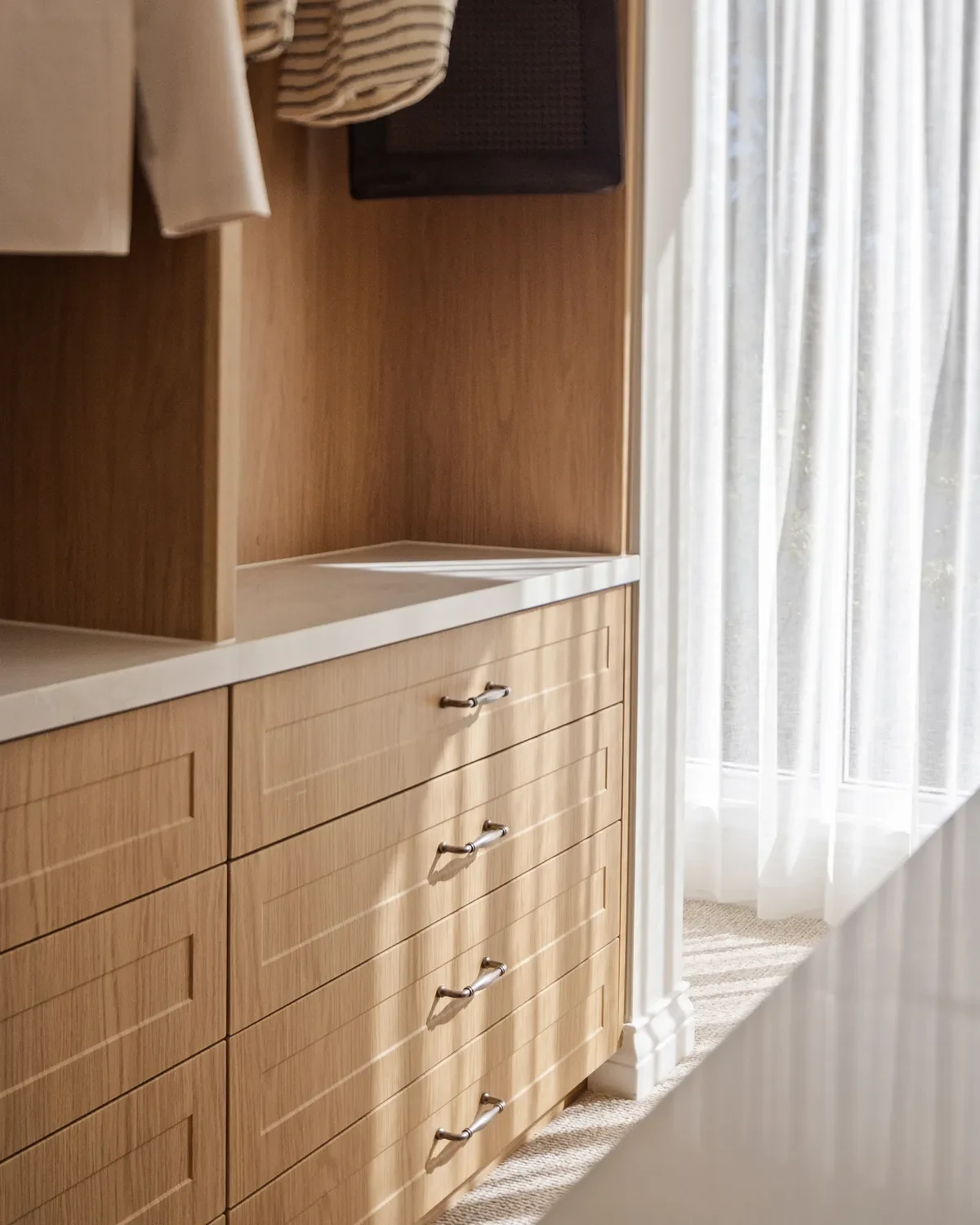 Walk-in robe in the Ashbourne display home with a Vevey Vanilla sheer curtain on the window beside timber drawers